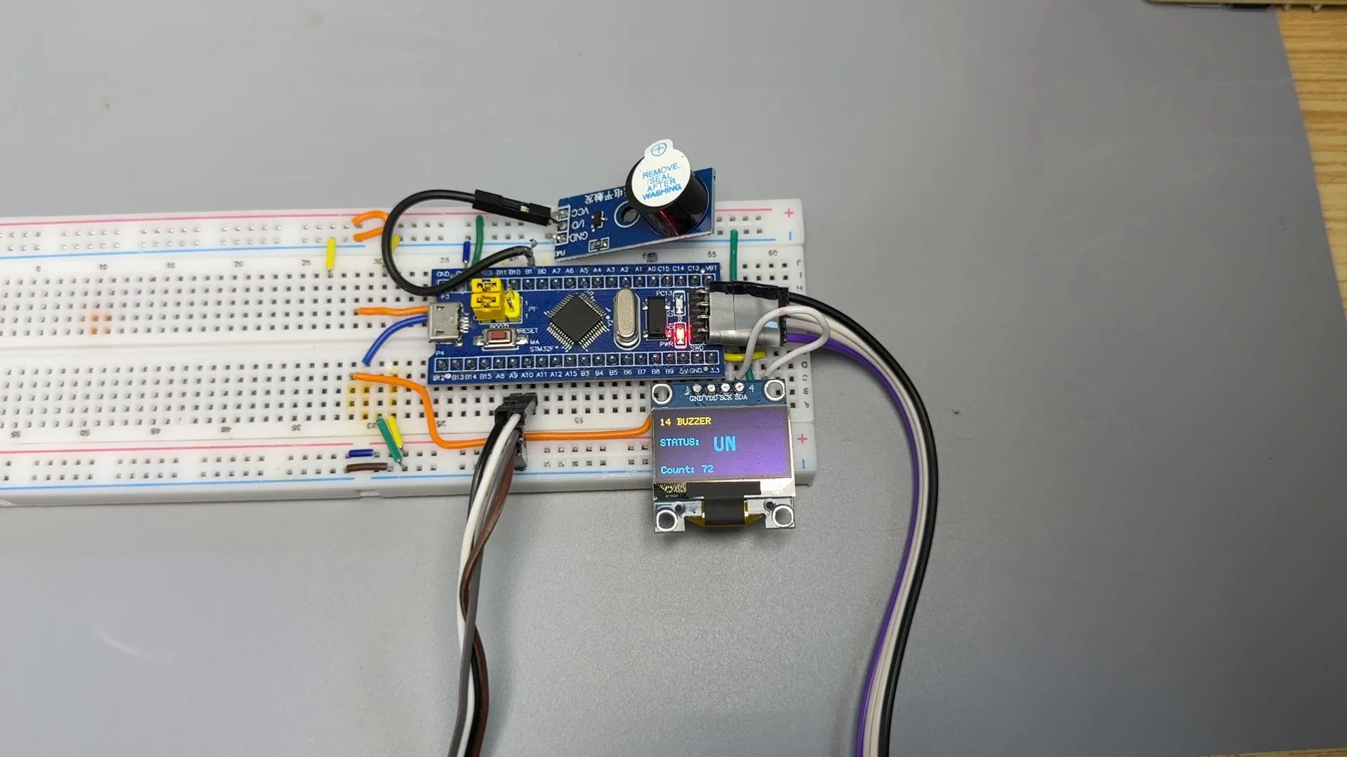 有源蜂鸣器实拍接线全景：模块 + 面包板 + STM32F103C8T6 + OLED 显示 STATUS ON