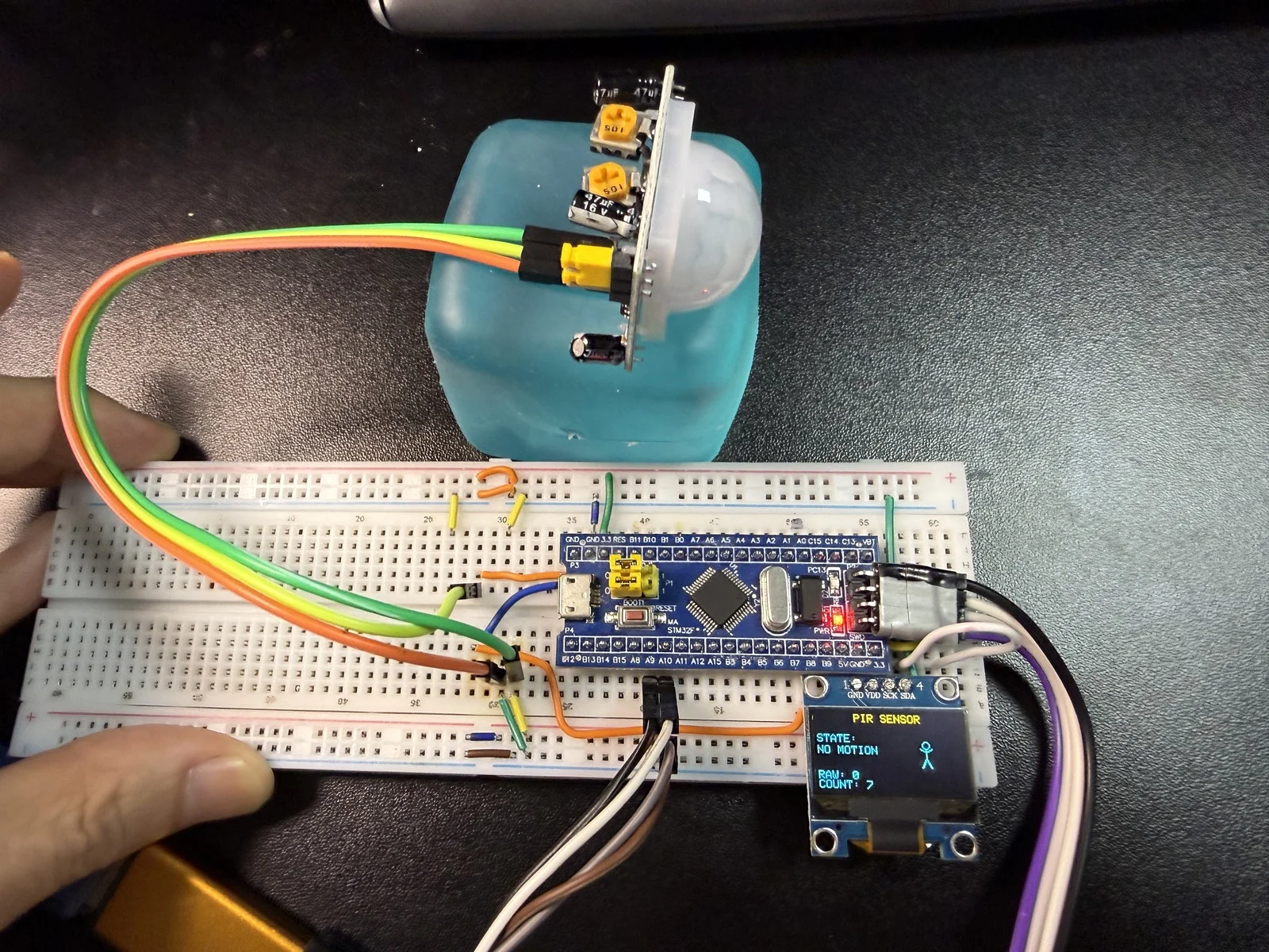 HC-SR501 实拍接线全景：模块 + 面包板 + STM32F103C8T6 + OLED 显示 NO MOTION，COUNT 已累计 7 次