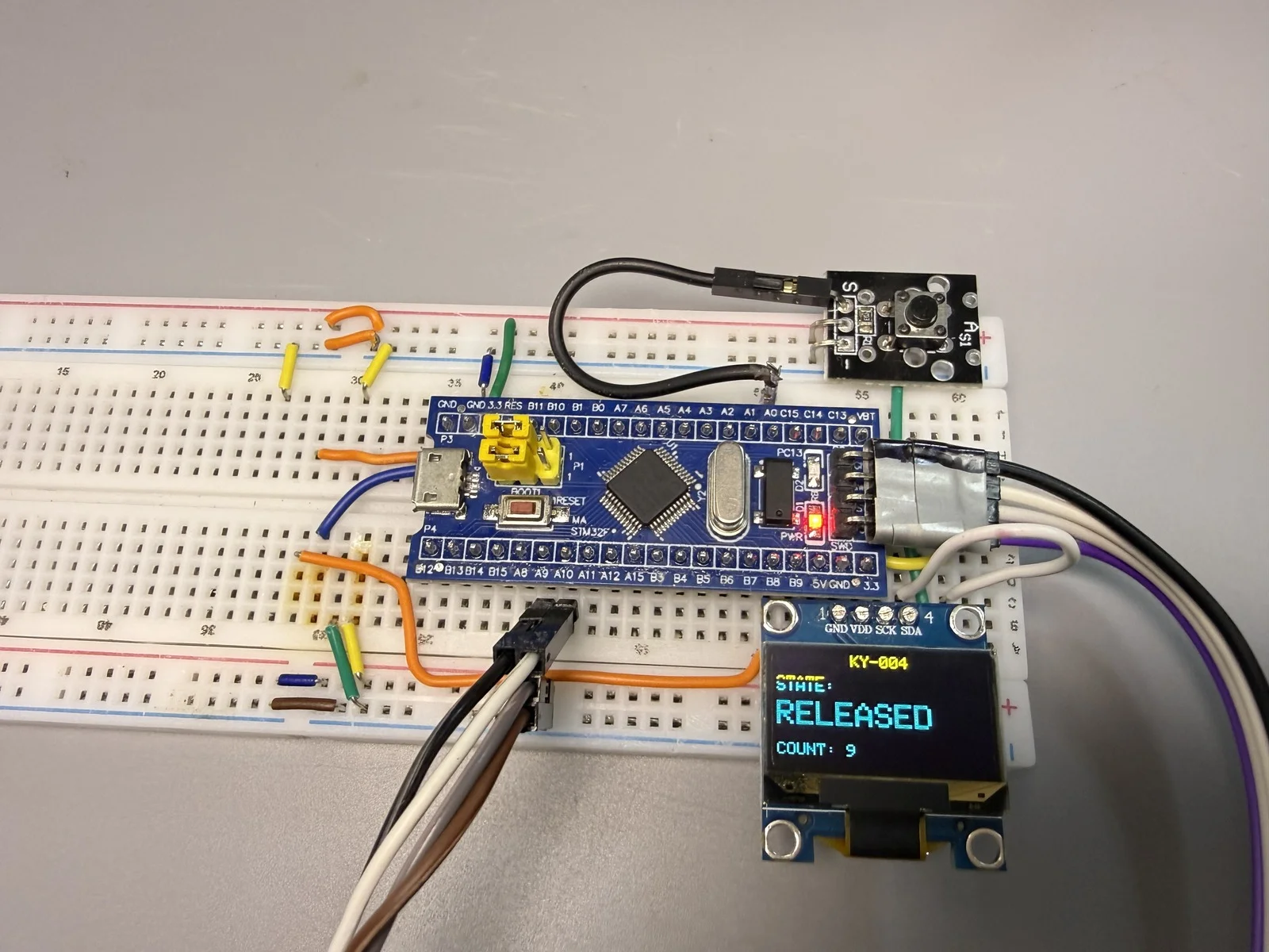 KY-004 实拍接线与结果：模块 + 面包板 + STM32F103C8T6 + OLED 显示 KY-004 / RELEASED / COUNT 9